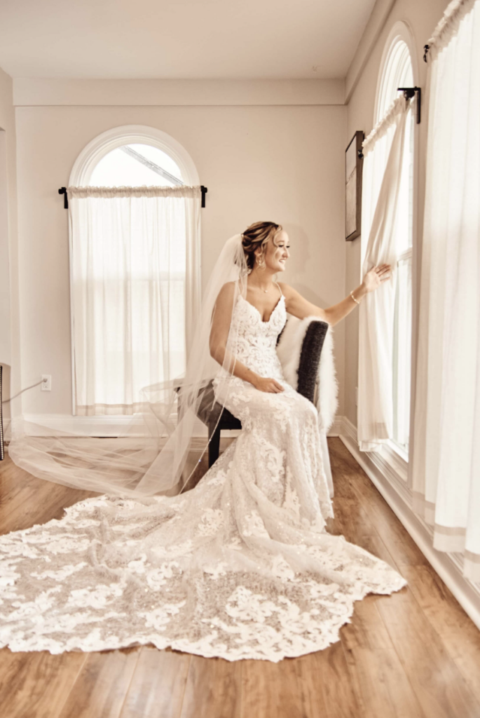 Bride sitting on bench looking outside inside of her getting ready AirBnB. 